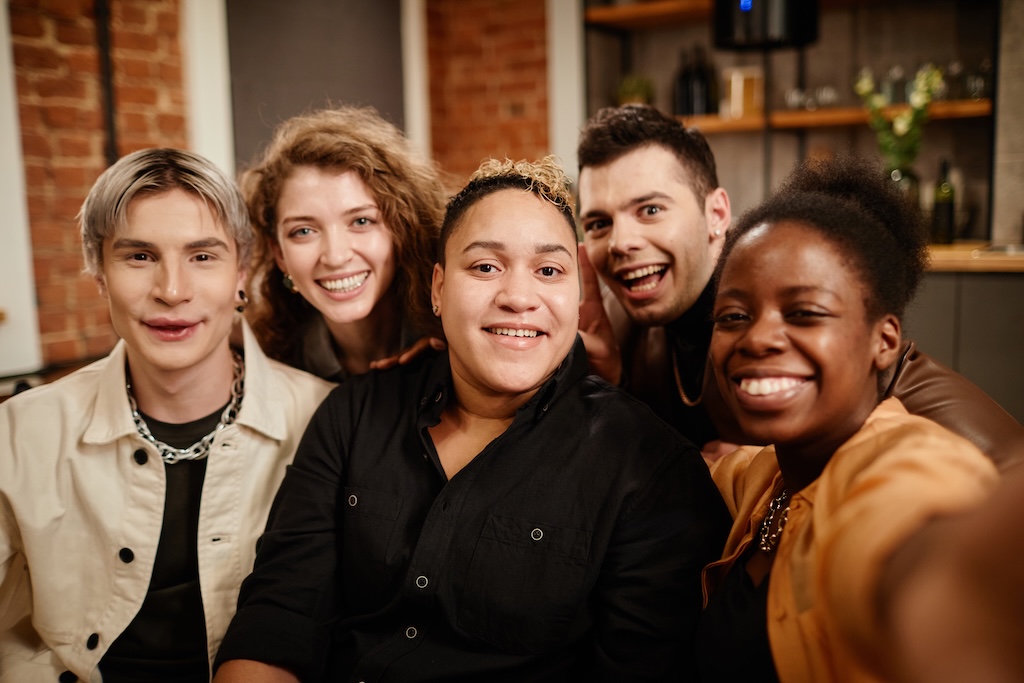 Group of young cheerful friends posing in front of camera while relaxing on couch in outpatient mental health treatment, which is what we offer at our center in San Diego.