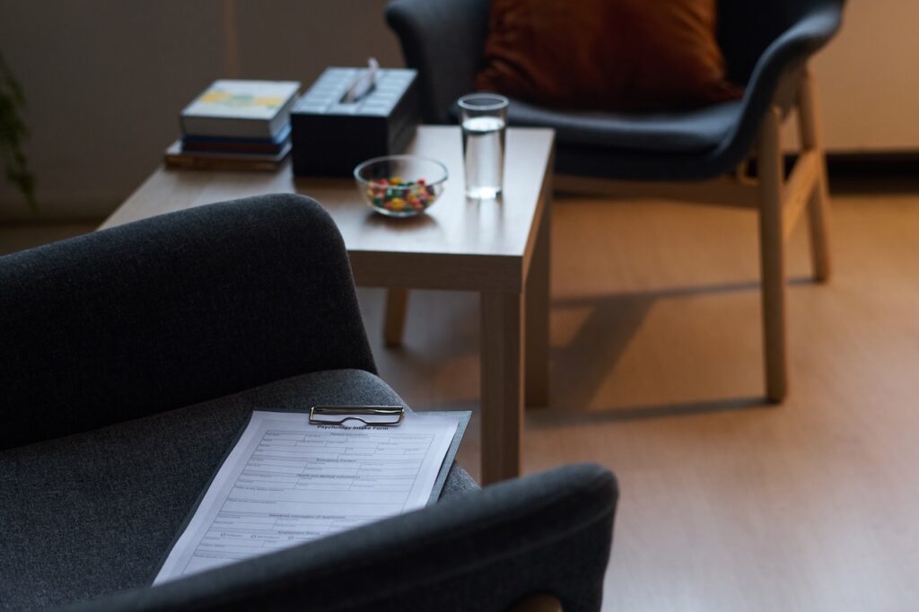 Clipboard with paper document lying on armchair against small square table in therapy office