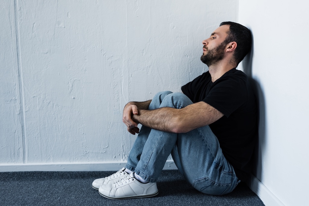 handsome depressed individual sitting on floor in corner by white wall and looking away