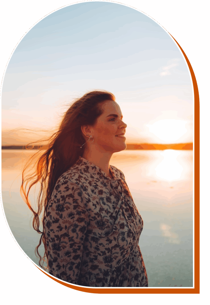 Young woman on the beach, looking out at the sunset