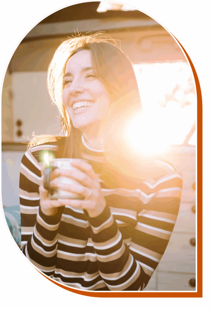 Young woman drinking coffee and smiling with sun shining across her face