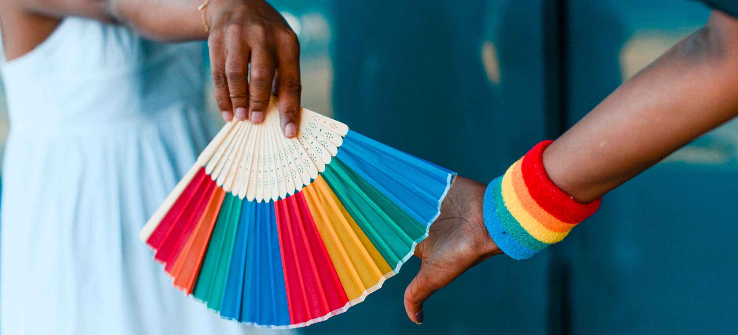 Two hands with a rainbow fan and wristband