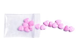 Closeup shot of a transparent ziplock bag and pink heart shaped pills on white background.