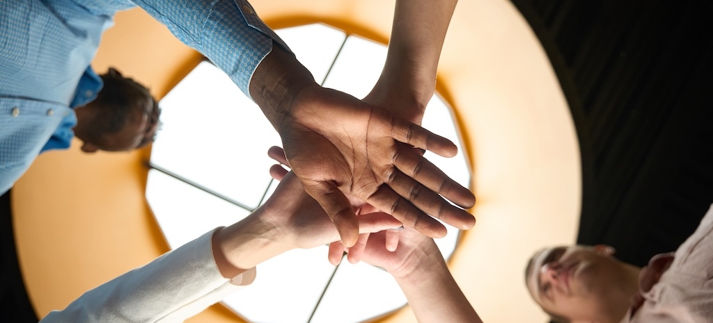Bottom view boss gathering his hardworking employees to work on project together, dedicated team putting hands together as symbol of friendly team
