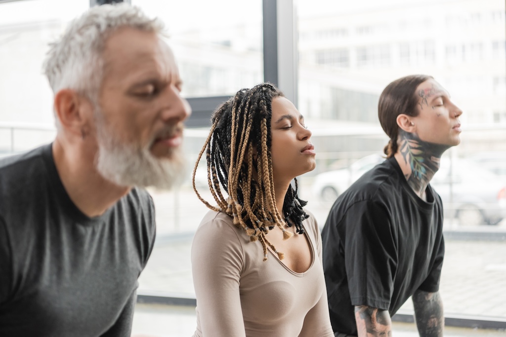 Three people meditating with closed eyes in yoga studio