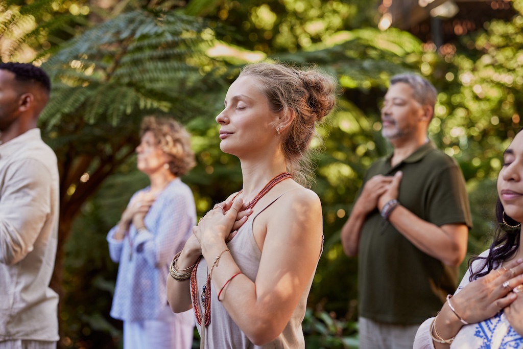 Multiethnic group of people standing outdoors with hands on their hearts, practicing mindfulness in a wellness retreat.