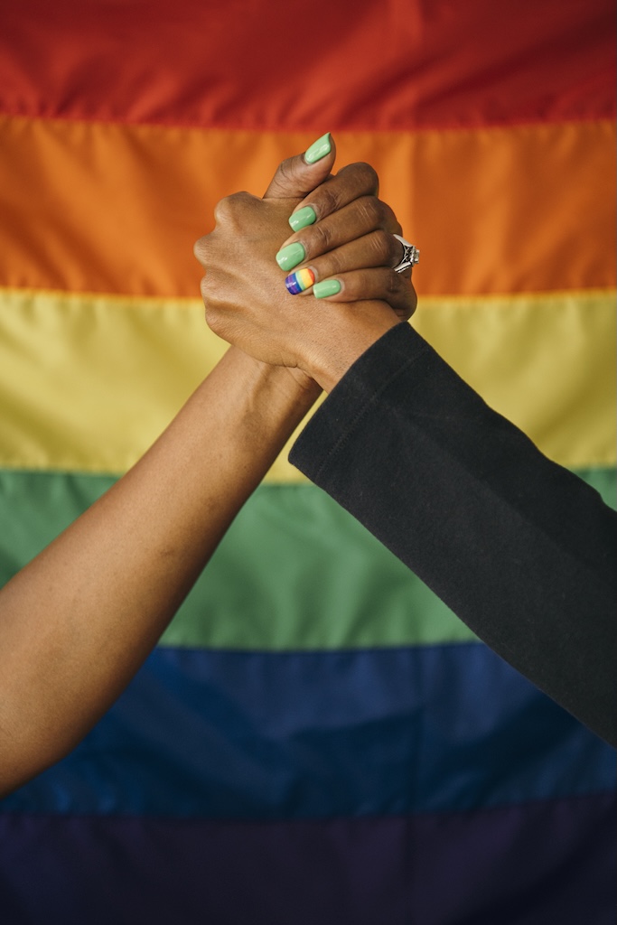 Gay couple holding hands in front of a rainbow flag signifying support and love