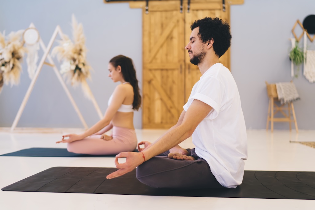 Side view of full body relaxed multiethnic friends in sportswear sitting in lotus pose on yoga mats while meditating in studio