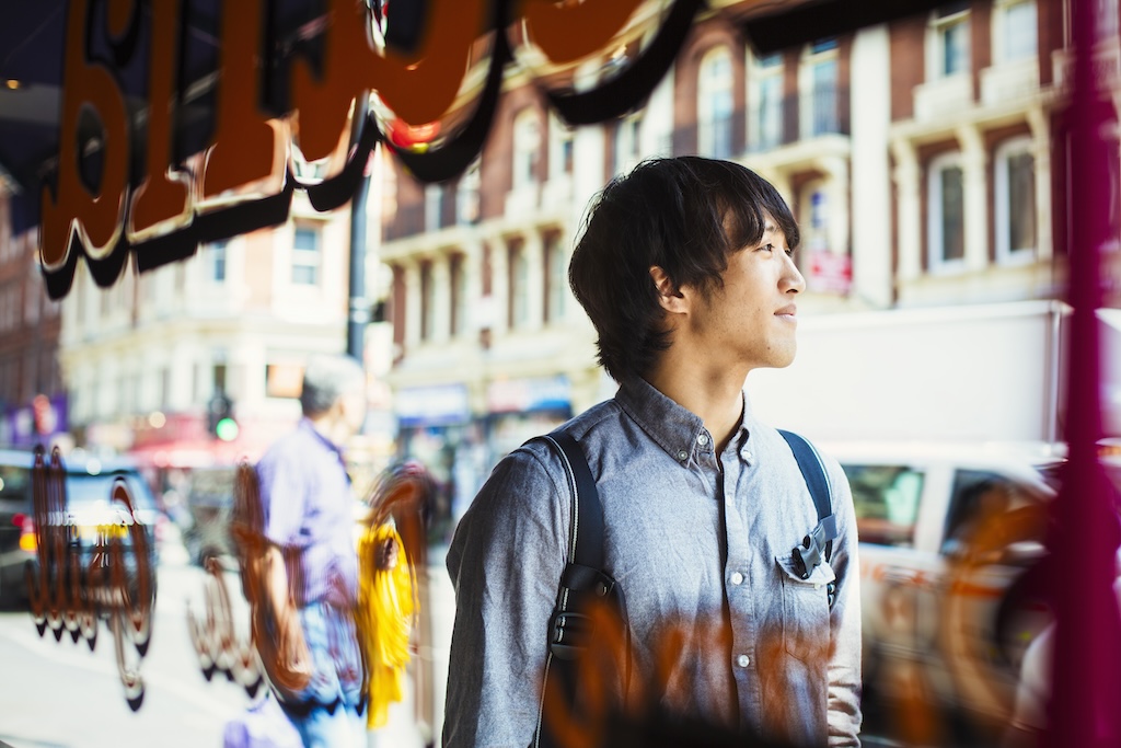 Young Japanese man enjoying a day out in London, walking past a shop window.