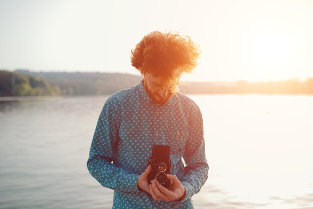 The red-haired guy in a blue shirt holding a medium format film camera in his hands and take photos near the lake