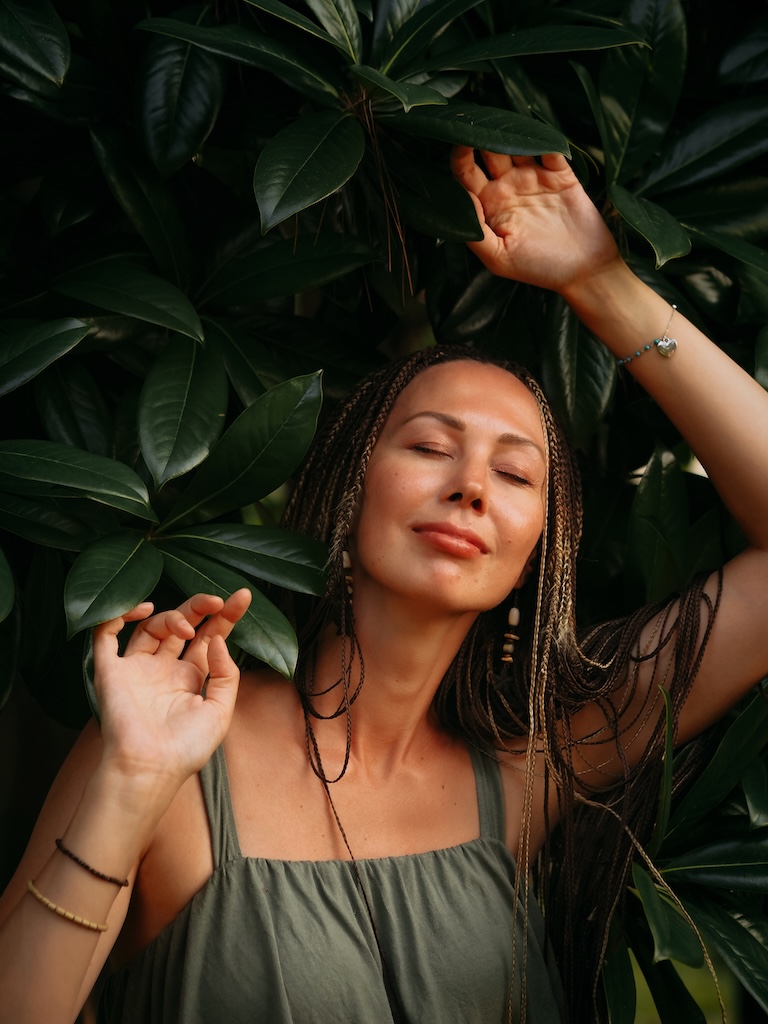 Woman with dreadlocks breathing deep surrounded by greenery and deep colored plants