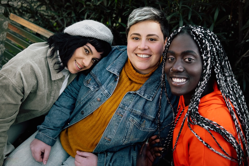 Group of three diverse women smiling watching the camera sitting on a bench at the park