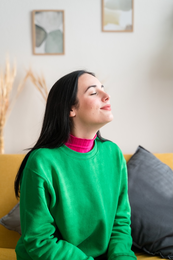 Side view of young female in casual clothes sitting on sofa and looking away while resting in cozy living room at home