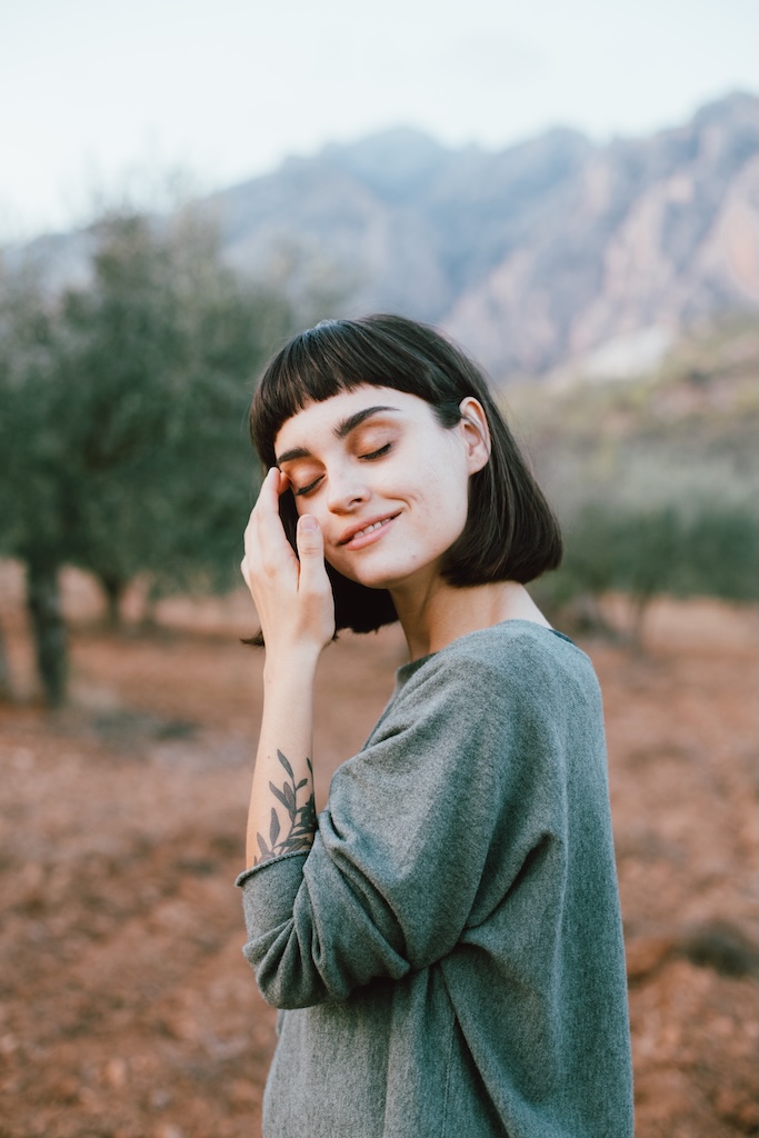 Portrait of woman or young traveling female smiling to camera, tranquil and calm while exploring national park forest with mountains and olive trees