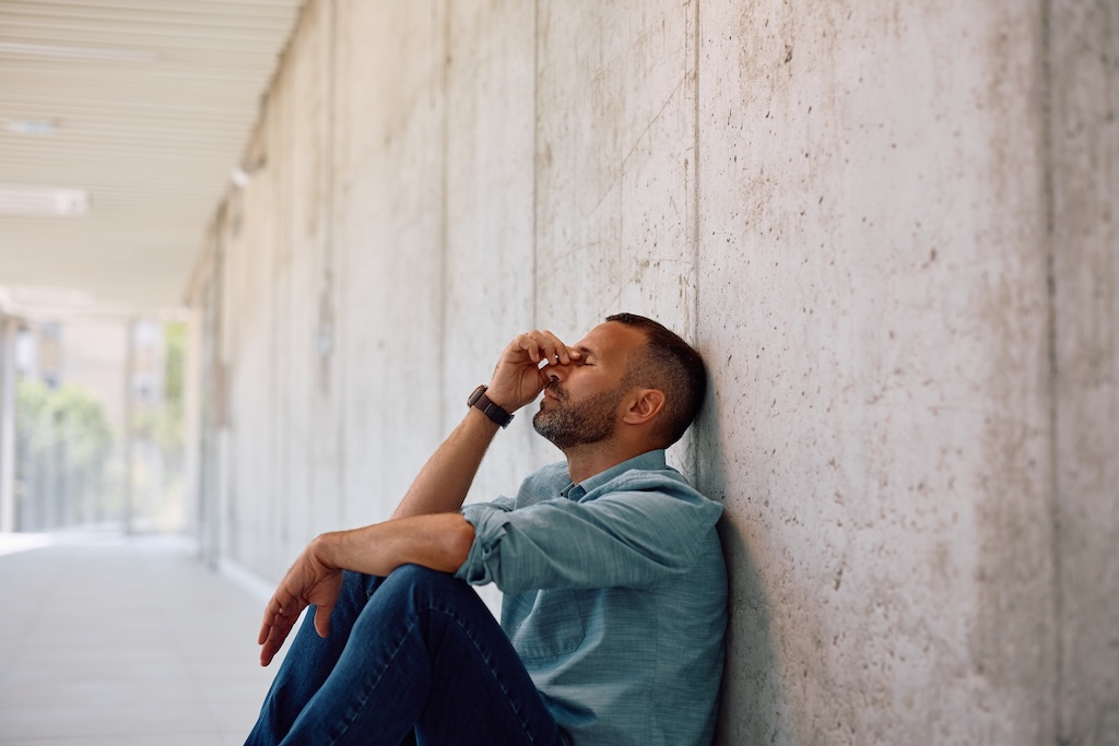 Tired businessman holding his head in pain while sitting on the floor in the office.