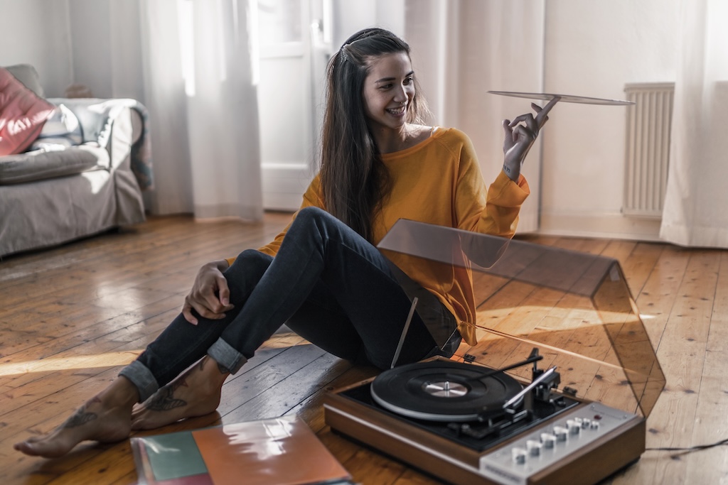 Smiling young woman sitting on the floor at home with record and record player