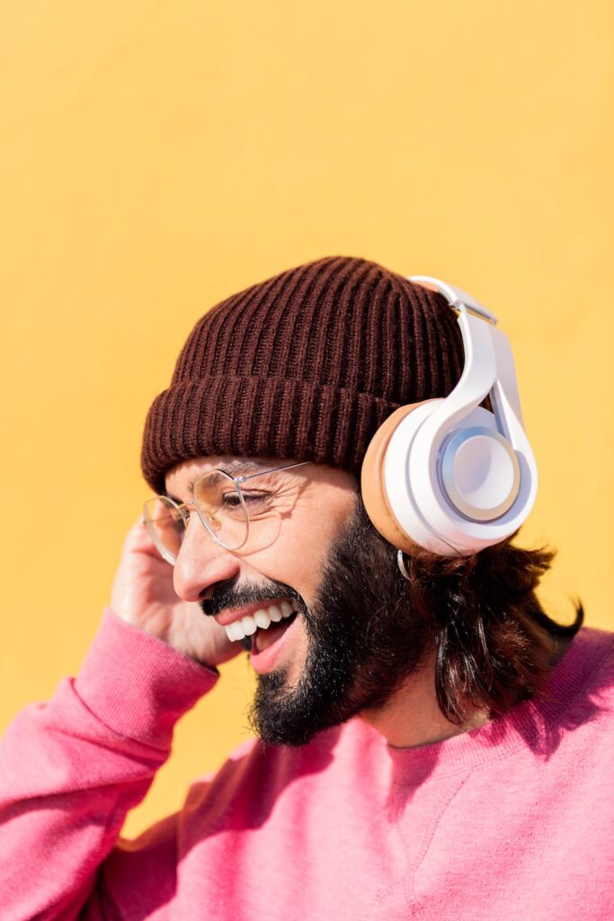 young man laughing listening to music on headphones with yellow background, concept of rhythm and positive people, copy space for text
