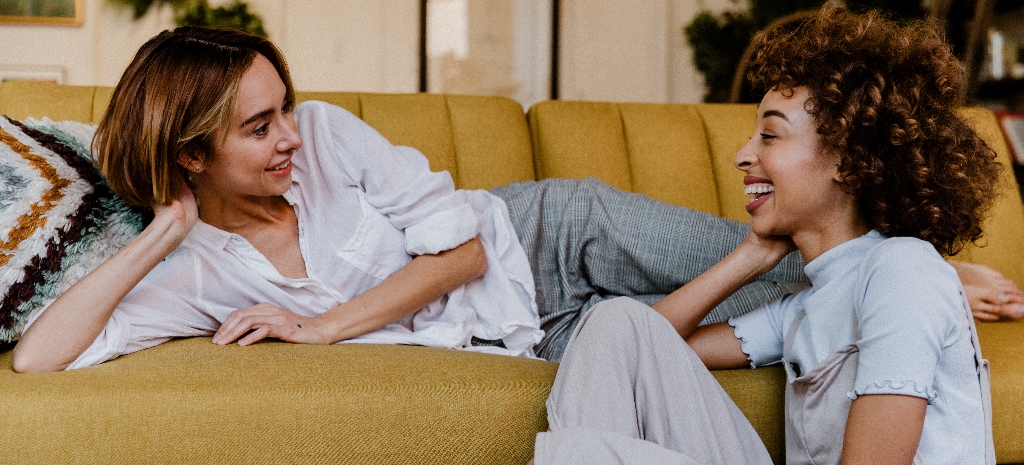 Two females, LGBTQIA couple sitting on the couch, smiling and chatting