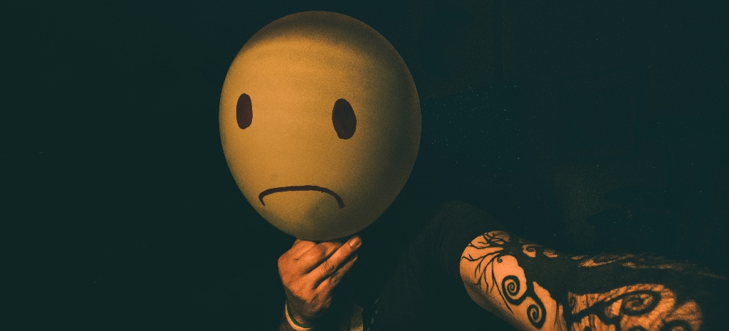 Man with tattooed arms holding a sad smiley face