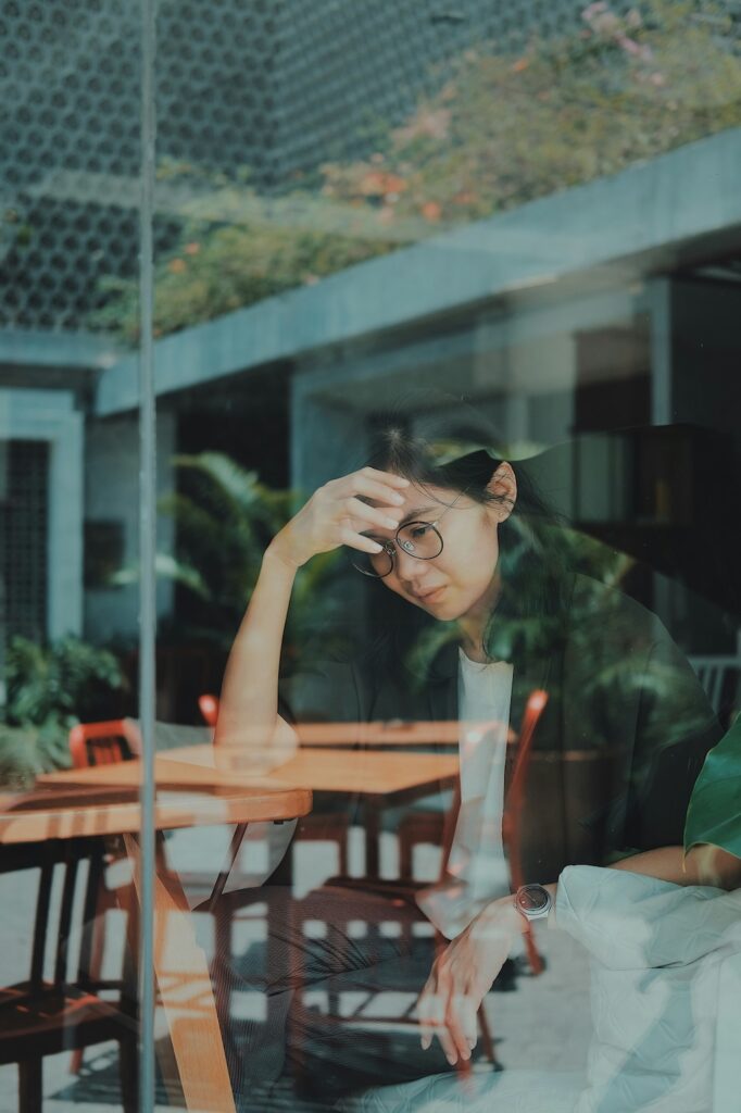 Individual sitting thoughtfully by a window, reflecting in a quiet moment, representing trauma recovery and mental health healing in a supportive, affirming care environment