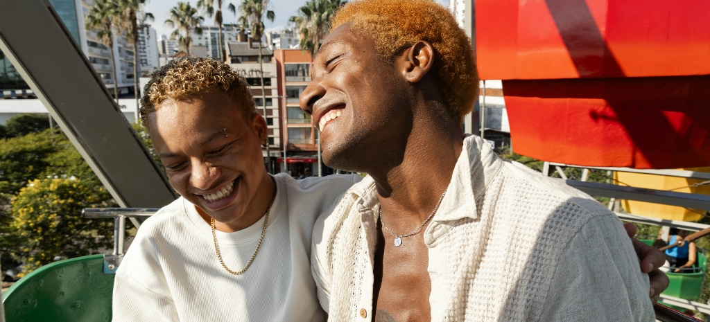 Two people smiling and leaning into each other outdoors, reflecting connection and support within an LGBTQIA+ affirming care environment