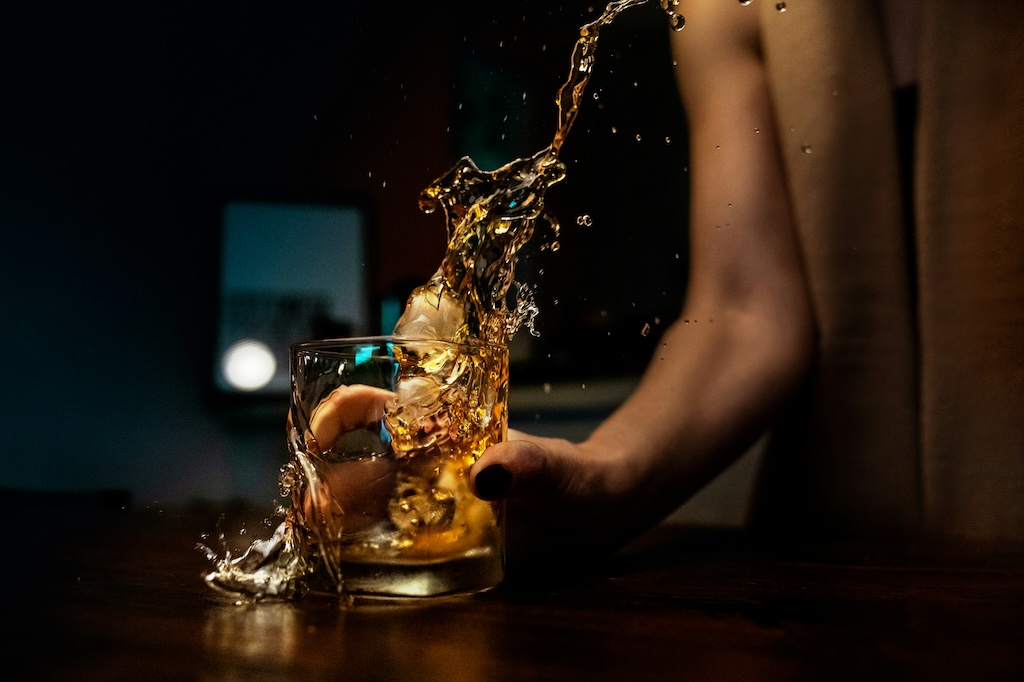 Hand holding a glass of whiskey mid-splash, representing active alcohol use in the context of seeking alcohol rehab in San Diego