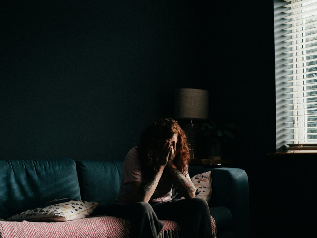 Person sitting on a couch with head in hands in a dimly lit room, reflecting emotional distress associated with cocaine addiction and need for treatment.