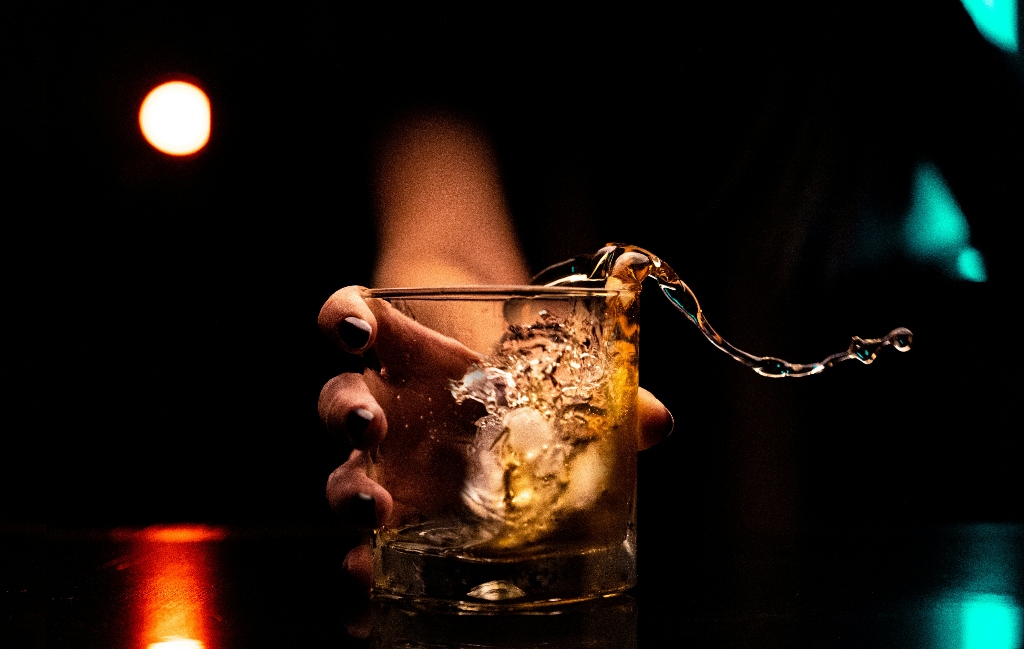 Hand holding a glass of whiskey as liquid splashes outward, representing alcohol use and how the body processes alcohol over time