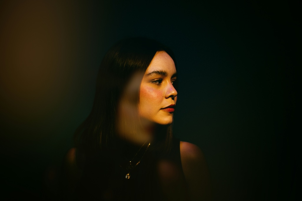 Person in soft, low lighting looking to the side with a reflective expression, representing gender dysphoria and self-reflection