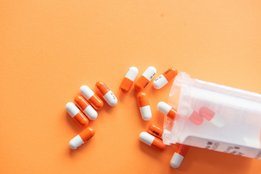 Orange and white prescription capsules spilled from a pill bottle, representing prescription drug use in an addiction treatment context