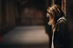 Person standing alone with head down in a dimly lit setting, reflecting emotional distress and isolation often associated with trauma bonding