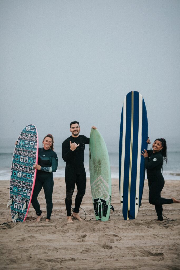 Three people standing together on the beach with surfboards, reflecting connection, community, and identity-affirming surf therapy at Element Q Healing Center.