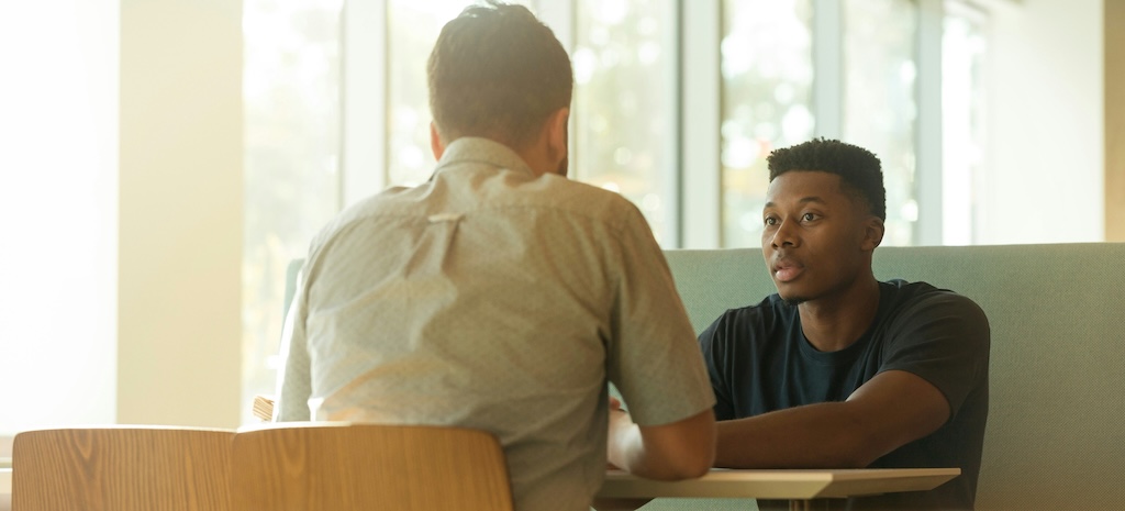 Young adult speaking with another person during a serious conversation about substance use concerns and heroin addiction warning signs.
