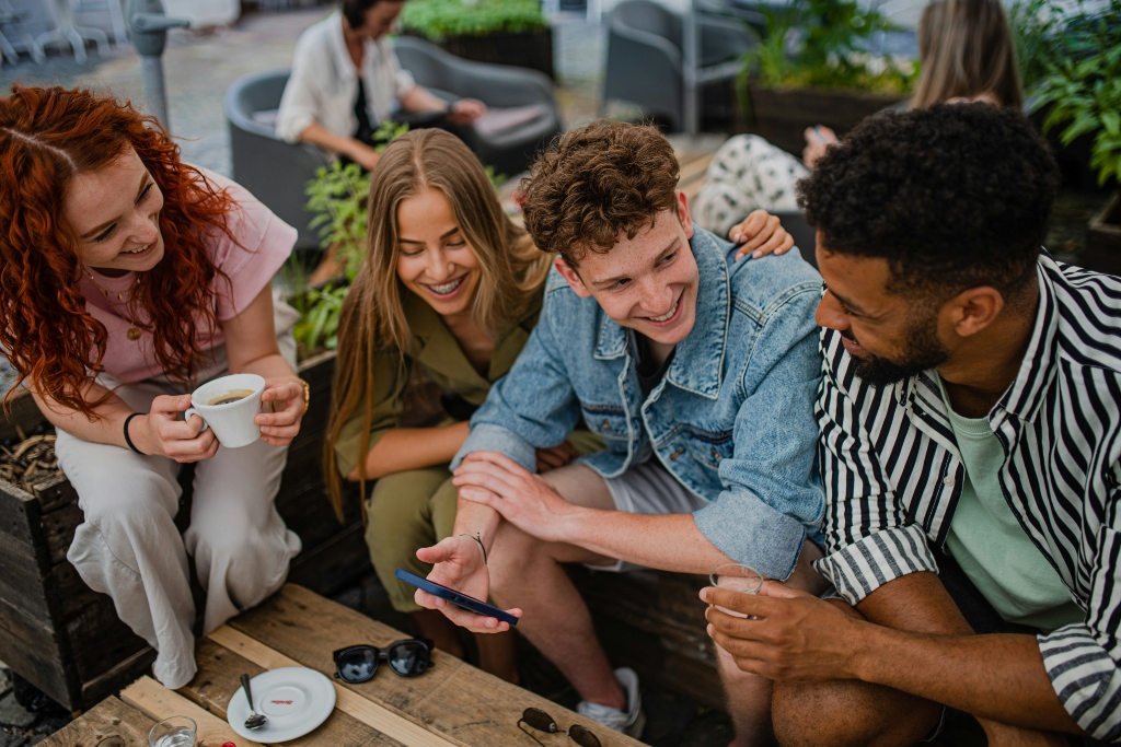 A diverse group of friends smiling and talking together outdoors at a café.