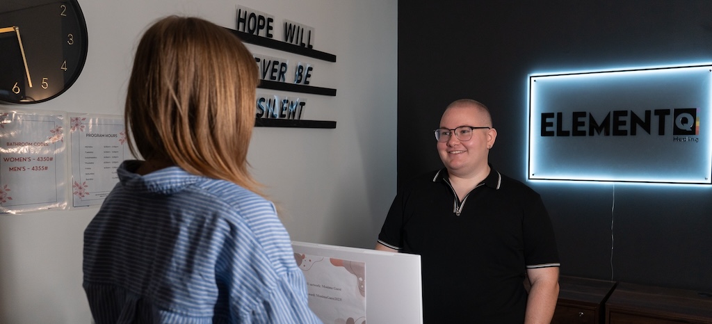 Element Q Healing Center staff member smiling while speaking with a visitor at the front desk.