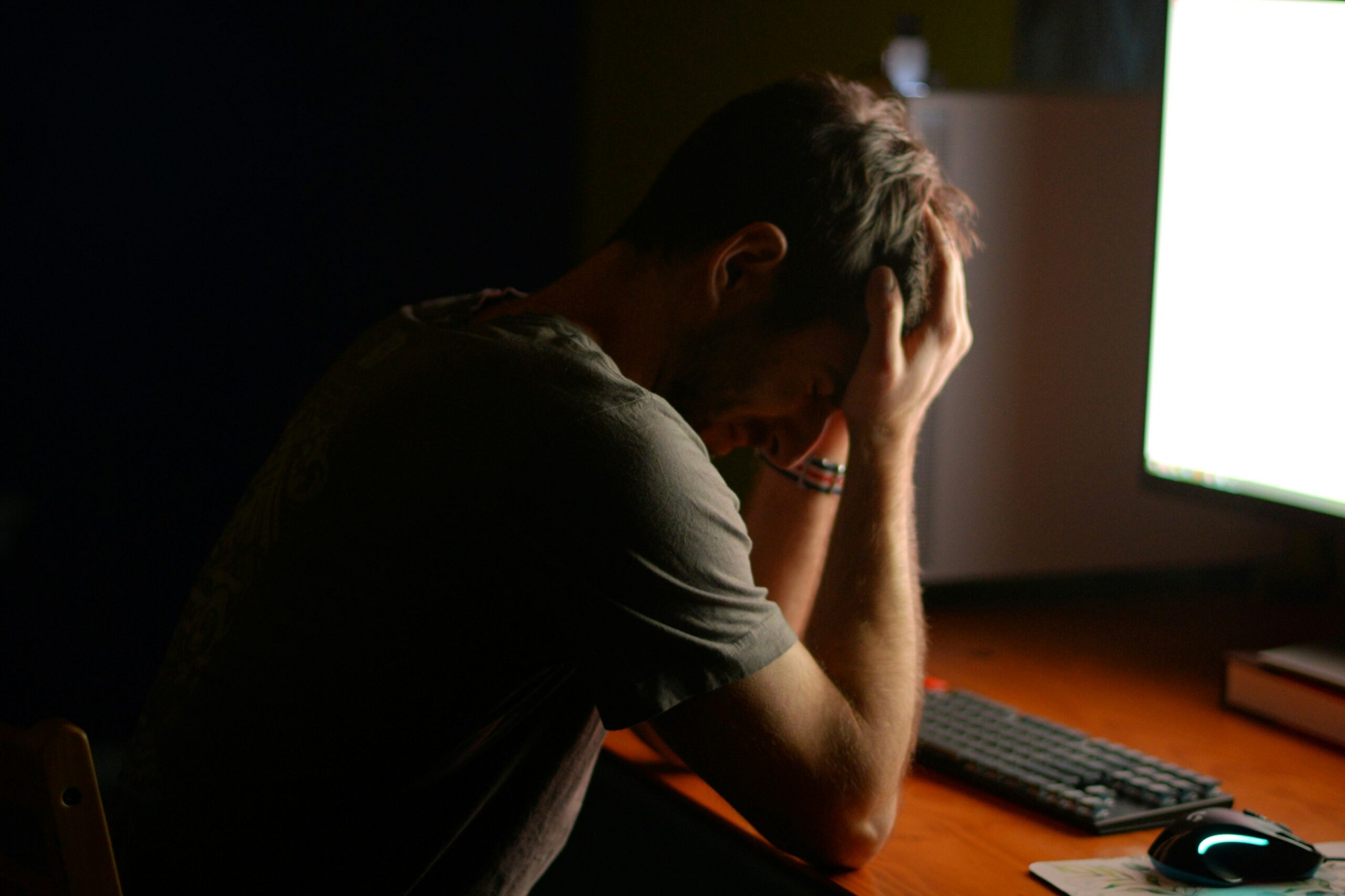 Person sitting at a computer with their head in their hands, appearing overwhelmed and exhausted.