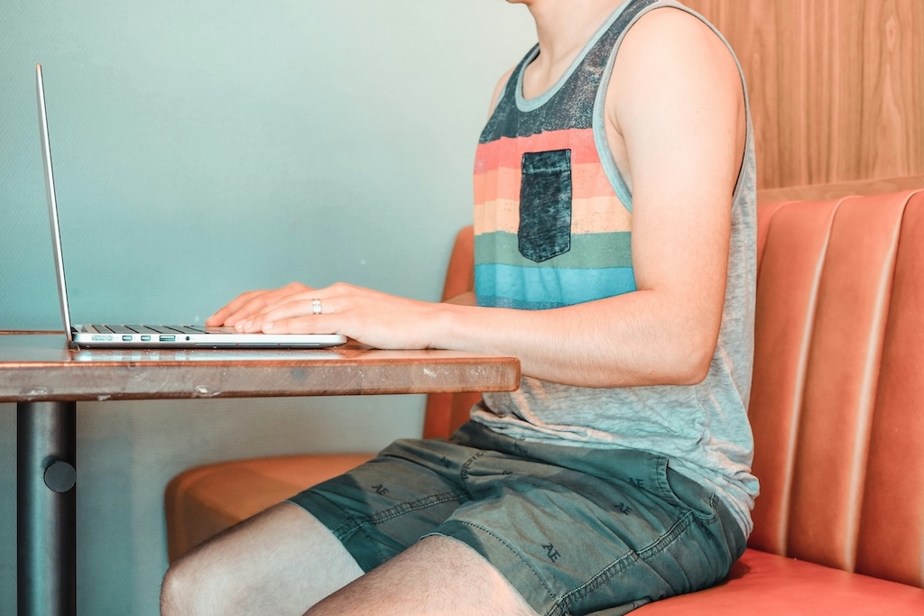 Person wearing a striped tank top and shorts while working on a laptop at a café.